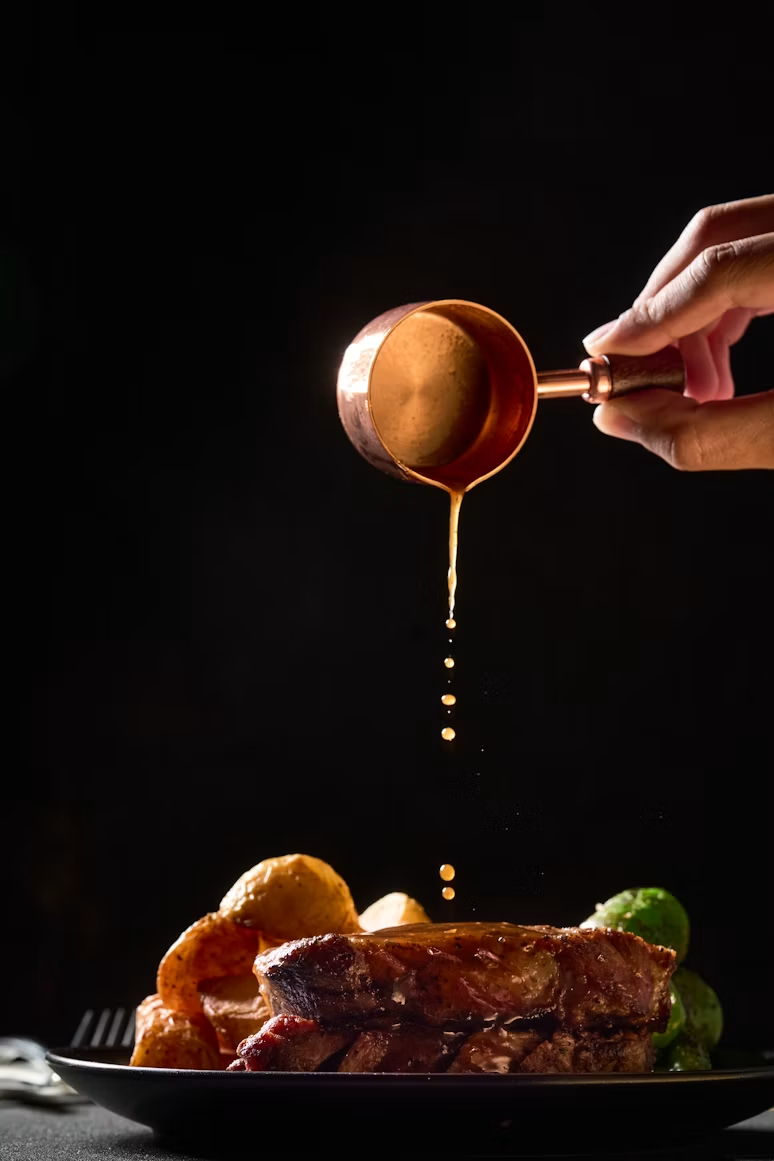 Gravy poured from a copper pan over a plated roast with potatoes and sprouts