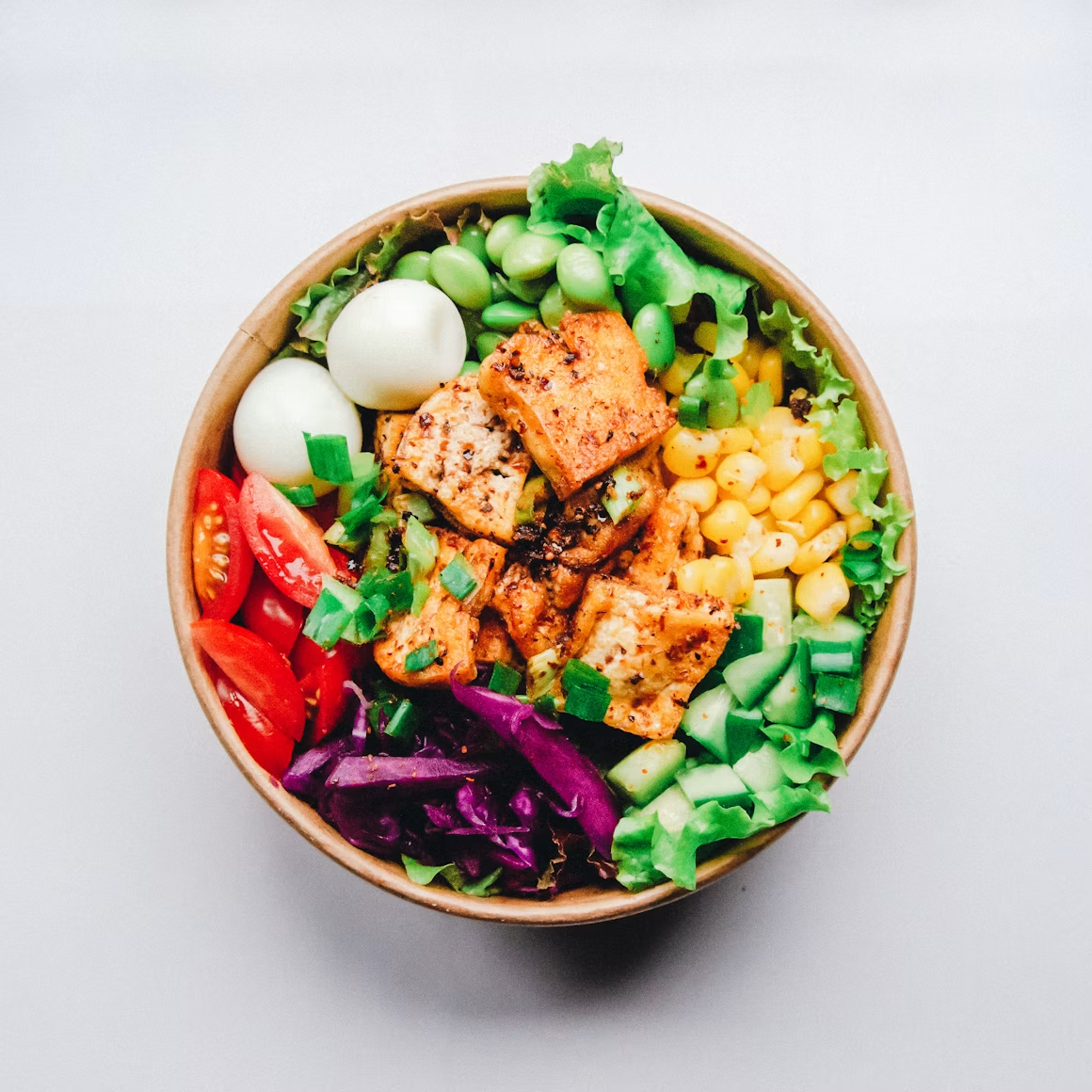 A bowl of chopped salad with seared tofu, corn, edamame, cucumber and halved eggs