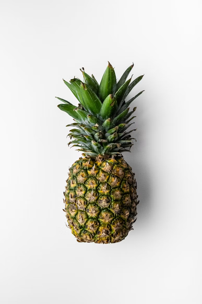 A whole pineapple lying on a pale surface, lit from one side