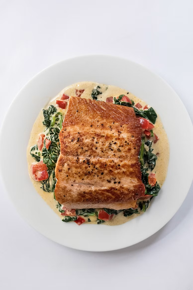 A seared salmon fillet on creamed spinach with diced tomato, plated on a white bowl