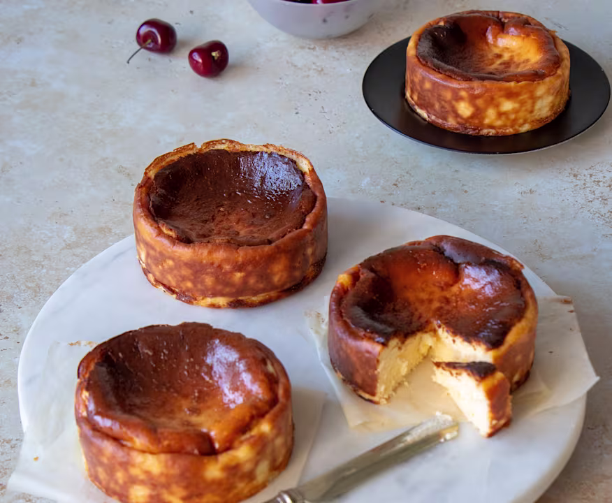 Four single-serve Basque cheesecakes with burnt tops, one cut open
